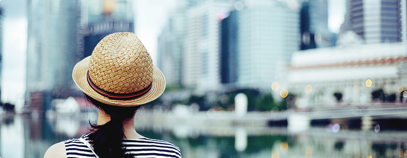町を眺める麦わら帽子をかぶった女性の後ろ姿の画像